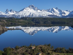 The snow-covered Mt. Cerro Castillo is reflected in a lake, small farm by the lake, Patagonia,