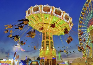 The colourfully illuminated Wellenflug chain carousel and the Ferris wheel in the evening, Cranger
