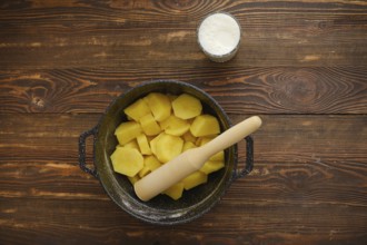 Top view of a kitchen table with boiled potatoes in a pot, potato masher and glass of warm milk