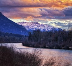 Mountain landscape at sunset with river, snow-covered peaks and dramatic cloudy sky, River Inn,
