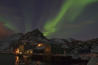 Night scene with northern lights in the sky, mountains in the background and illuminated houses on