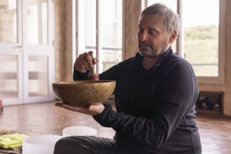 In a serene room, a mature man sits calmly, with a serene expression as he gently plays a bronze