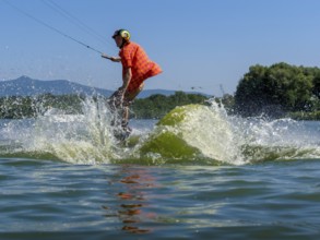 Young casual man with flapping shirt on wakeboard jumping into the lake, water ski and wakepark,