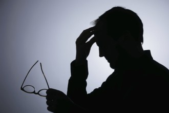 Symbolic photo on the subject of overload. Silhouette of a man rubbing his aching head. Berlin,