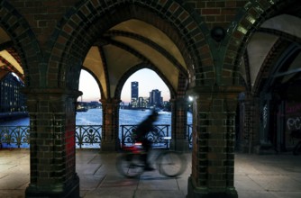 Bicycle rider to the sunrise at the Oberbaum Bridge, view through the arcades over the Spree to the