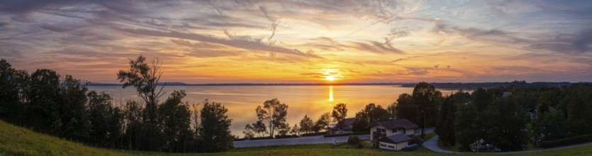 Sunset over a lake with a calm atmosphere, surrounded by trees and a slightly cloudy sky, Chiemsee