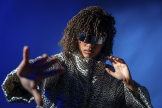Fashionable woman with curly hair wearing futuristic sunglasses and striking a pose on a vibrant