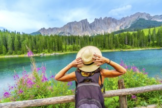 Female hiker with backpack holding her straw hat while admiring the turquoise waters of lake