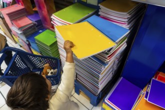 A child is reaching for a yellow spiral notebook in a store. The store is filled with many