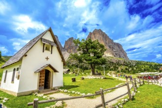 Tourists enjoying a sunny day at sella pass, with the chapel and the sassolungo group in the