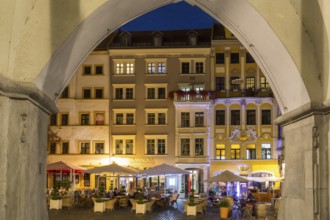 View through the arches of the arcades of the hall houses to the row of street cafés at night,