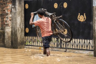 A person carries a bicycle as he wade through a flooded street after heavy rains in Guwahati, India