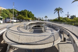 Modern pedestrian bridge with circular paths and palm trees in sunny weather, Seville