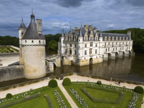 Frontal view of an imposing castle on the river Cher with manicured gardens and dramatic cloudy
