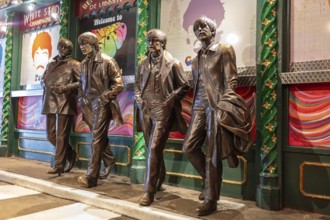 Four bronze statues depict people in motion in front of a decorated block, Liverpool