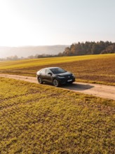 A car drives alone on a country lane, surrounded by golden fields under the sun, electric car VW