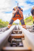 Two construction workers working on the rails, looking along the tracks in a rural setting, rail