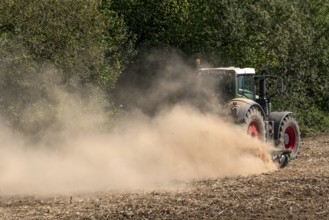 Tractor with plough digging up dried-out soil, large cloud of dust, dust, dry, field, earth,