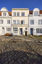 Historic houses, facades with windows, roofs with red roof tiles and dormers, cobblestone pavement,