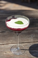 Elegant dessert in a glass with red raspberry sauce, white cream and mint leaf on a wooden table,
