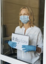 Woman with medical mask holding stay home notebook window