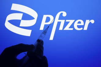A gloved hand holding a syringe in front of the pfizer logo. Pfizer Inc. is an American