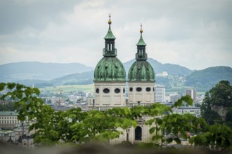 Two church towers with green roofs, framed by leaves, landscape in the background, Salzburg,