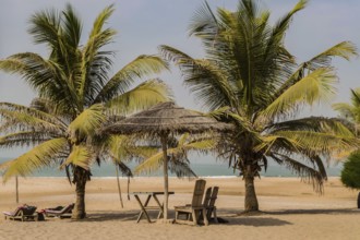 Two chairs and coffee table under a palm leaf and wood parasol on Bijilo Beach in The Gambia