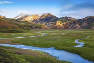 Snow lies in the hollows of colorful rhyolite mountains. Green Valley is flooded with melt water.