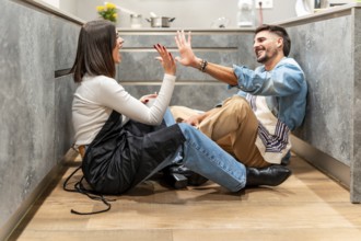 Two young chefs are sitting on the kitchen floor, giving each other a high five and laughing,