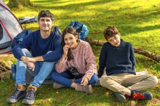 Happy caucasian father, daughter and son sitting next to camping tent enjoying nature in the forest