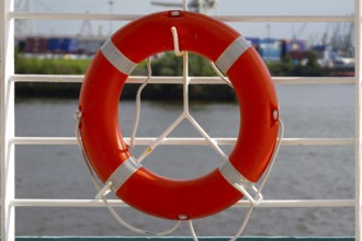 An orange lifebuoy hangs from a white railing with a view of a harbour, Hamburg, Germany, Europe