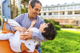 Grandfather holding and playing with his grandson at the playground, they are laughing and having