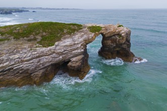 Rocky arch on the coast above the roaring ocean with green-blue water, aerial view, Praia das