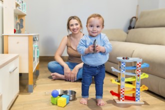 Adorable baby boy playing with a toy cymbal while mother sits on the floor, capturing a