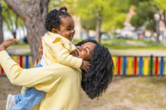 Joyful mother and adorable african girl embracing playing on a park