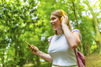 Happy caucasian young woman using phone and enjoying music in the nature while trekking in the