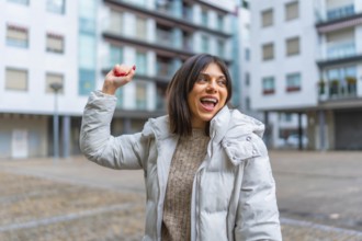 Happy woman wearing winter jacket raising hand while dancing in the city