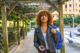 Latin young woman walking with rucksack while using smartphone to find a direction in the city