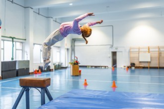 Girl practicing backflip in school gym, showcasing flexibility and athleticism during physical