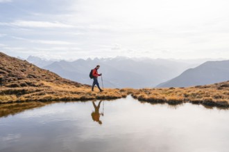 Mountaineer hiking with poles, reflected in a small mountain lake on the Krahberg, mountain