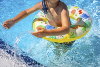 Part of a playful boy on a pool playing with colorful rubber ring