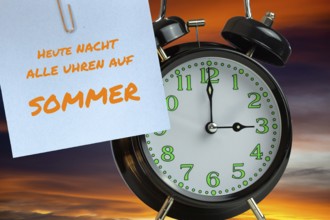 (Photomontage) Summer time changeover Symbolic image: Alarm clock in front of evening sky and text