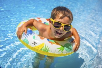Boy having fun in the swimming pool with a floating rubber ring in summer