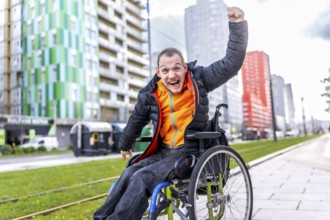 Happy disabled man celebrating raising his fist while sitting in a wheelchair in a city street