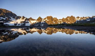 Rocky mountain peaks reflected in a small pond, mountain landscape with alpenglow at sunrise, at