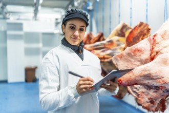 Female butcher making quality report writing notes in a clipboard in meat processing factory