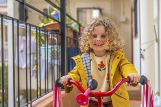 Close-up of a smiling little girl playing riding bike in the terrace at home