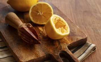 Lemons and a wooden manual citrus juicer, on a chopping board, close-up, no people