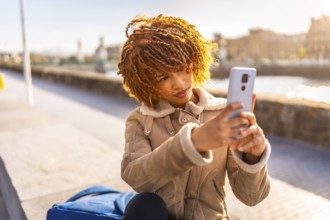 Latin young woman taking photo with mobile phone of a beauty sunset on the river in the city